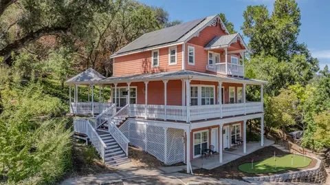 Two-story home with wraparound porches among oak trees